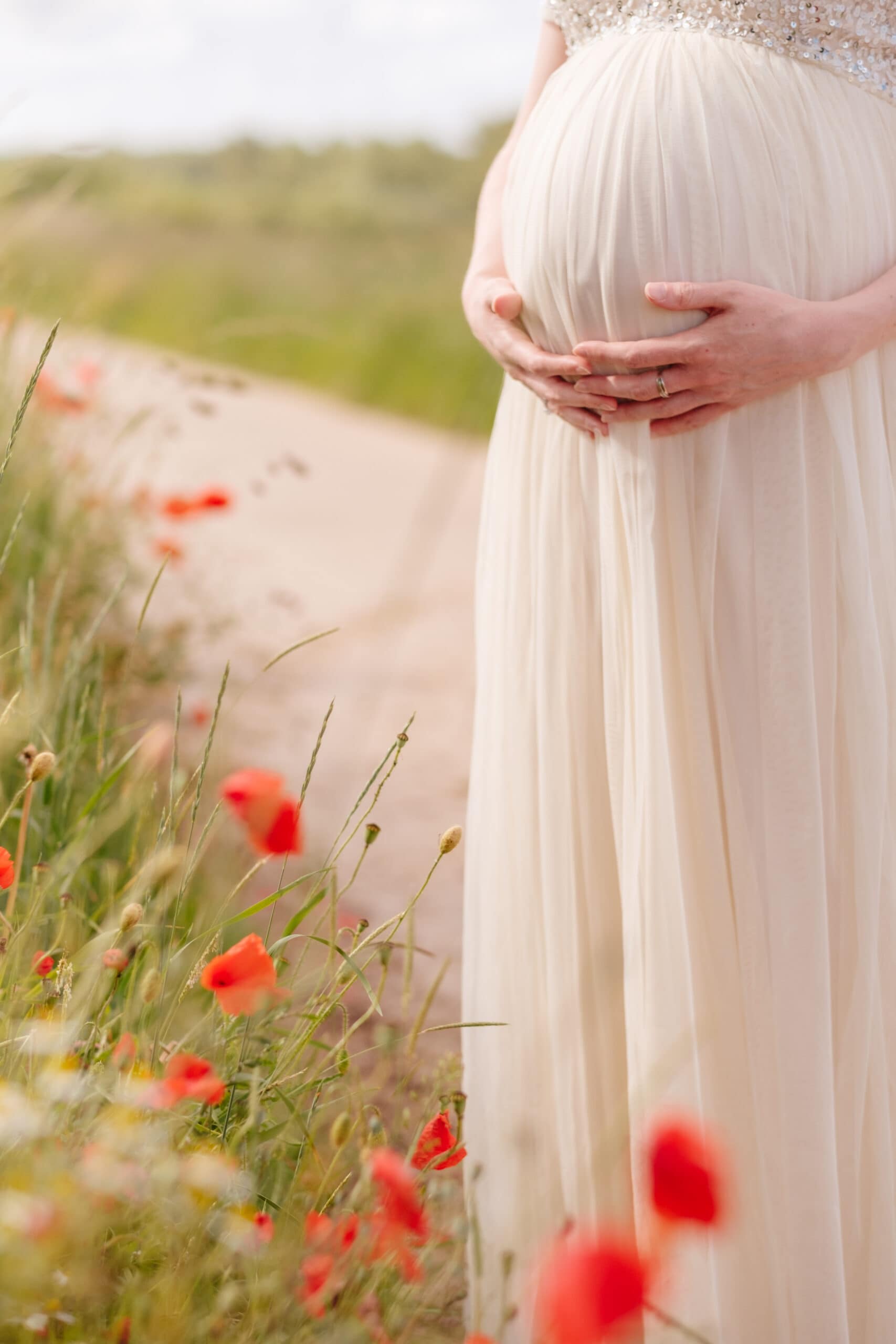Detail van zwangere buik en klaprozen op de achtergrond