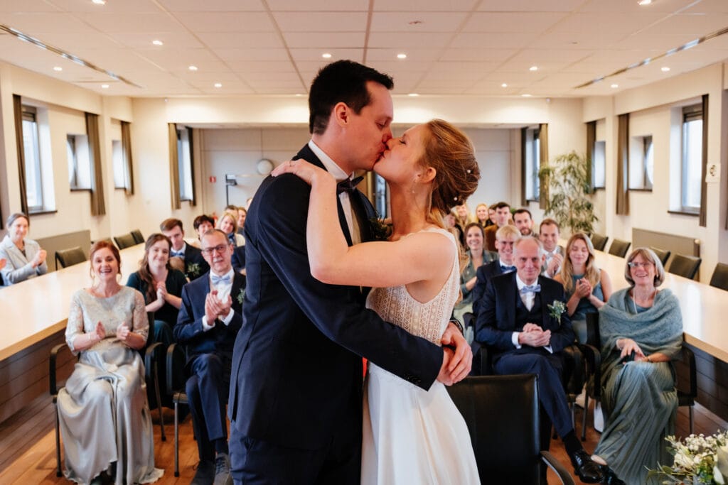 Bruid e bruidegom kussen elkaar in gemeentehuis Lubbeek bij bezegeling van hun huwelijk